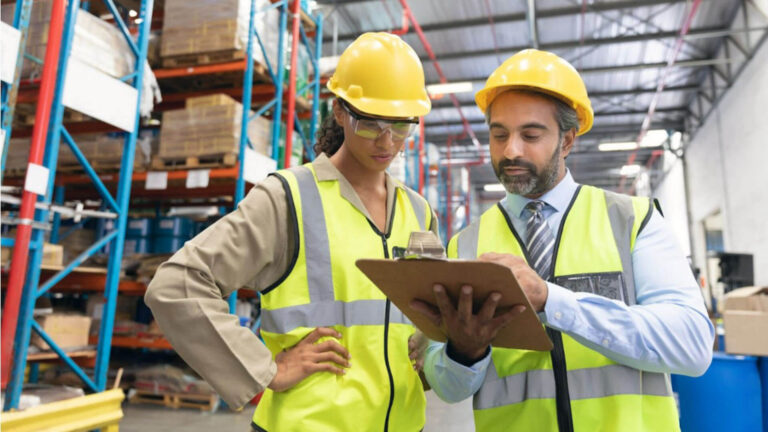 Male and female staff discussing over clipboard in warehouse
