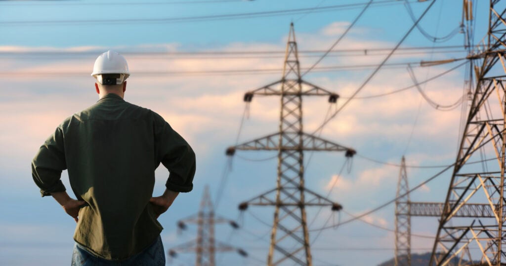 High-voltage power lines and an engineer in safety gear inspecting infrastructure.