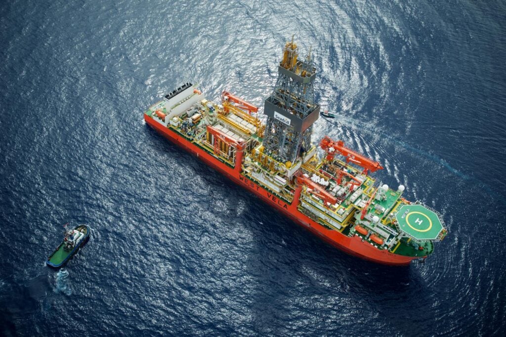 Offshore oil rig with associated supply vessel on deep blue ocean.
