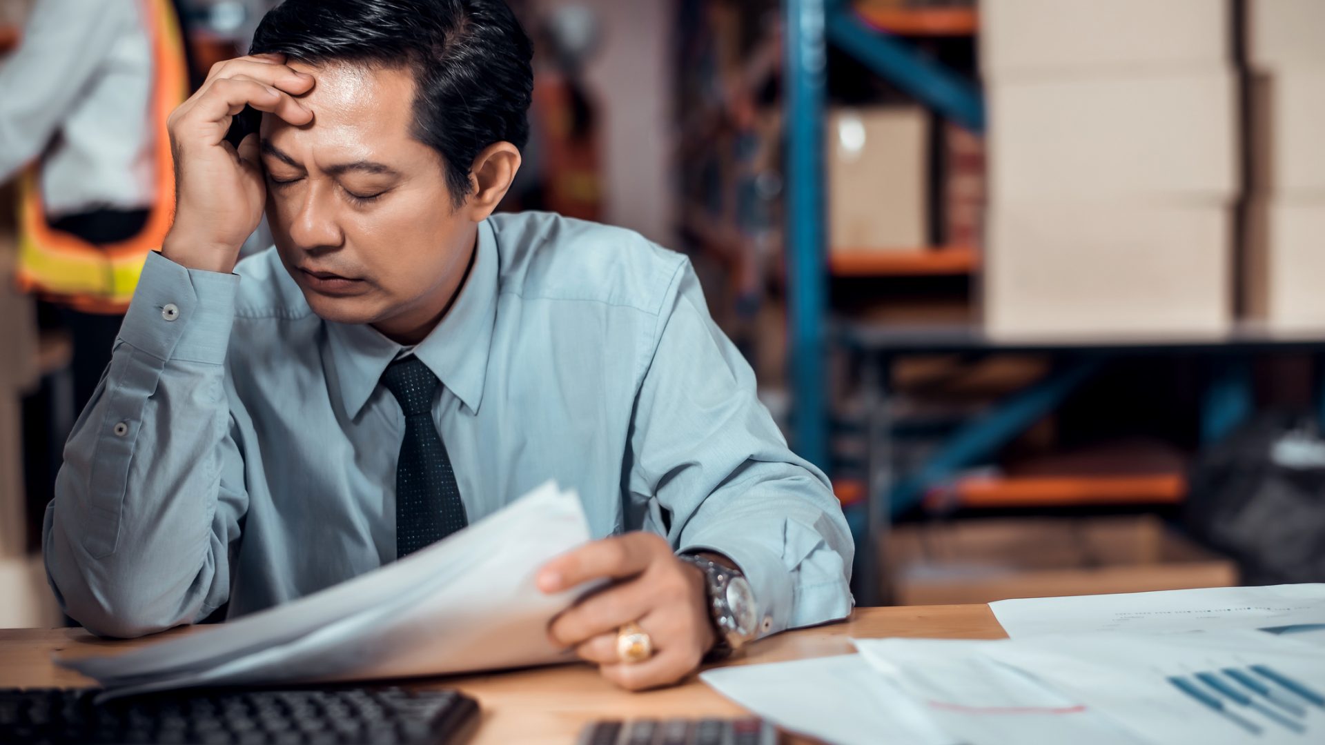 Stressed businessman worry about financial balance trouble of his company at his office in warehouse. Profit less than target while global corona virus or Covid-19 crisis, negative emotional concept