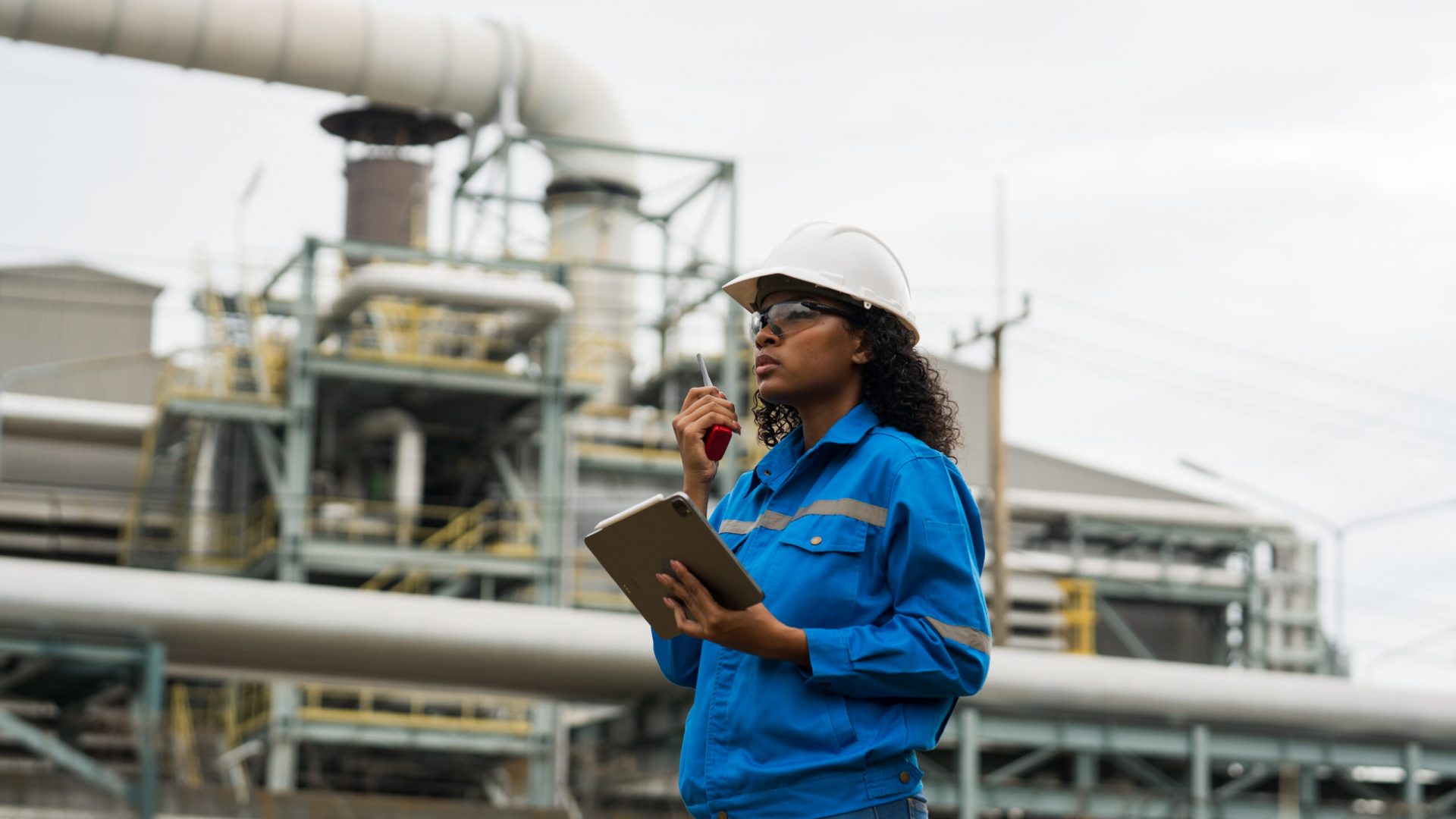 Female engineers work with walkie talkie in gas refineries and oil refinery plants to check production quality and safety of refineries.
