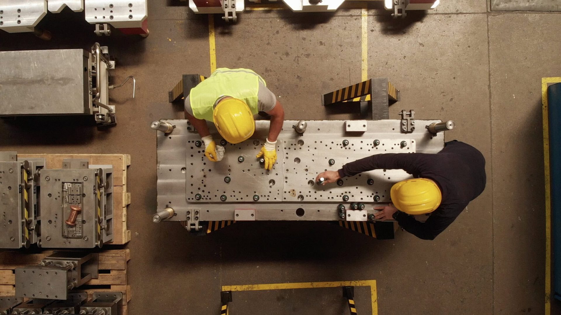 High-angle view of two workers in yellow helmets inspecting industrial equipment in a manufacturing.