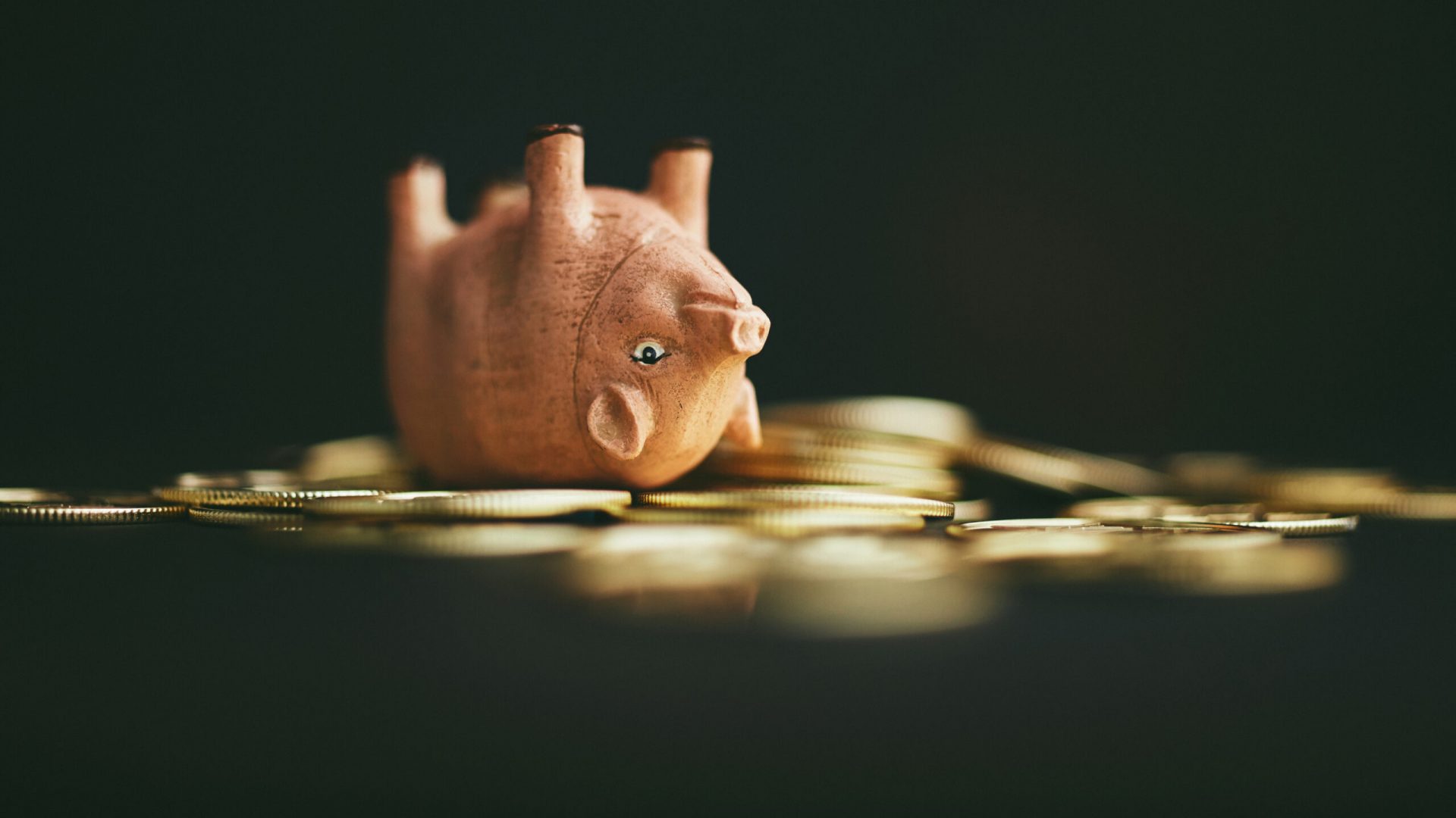 Cute pink pig upside down on a pile of gold coins. Rolling in dough or money