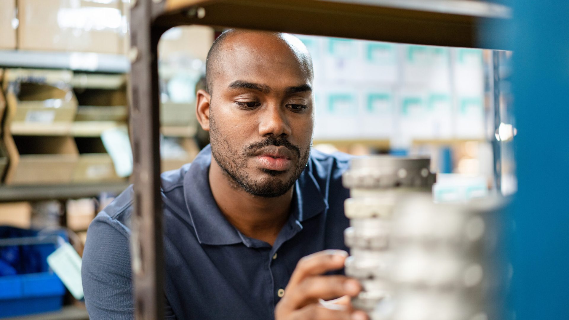 Young african man checking the material on storage rack in warehouse. Male worker examining goods in distribution warehouse racks.