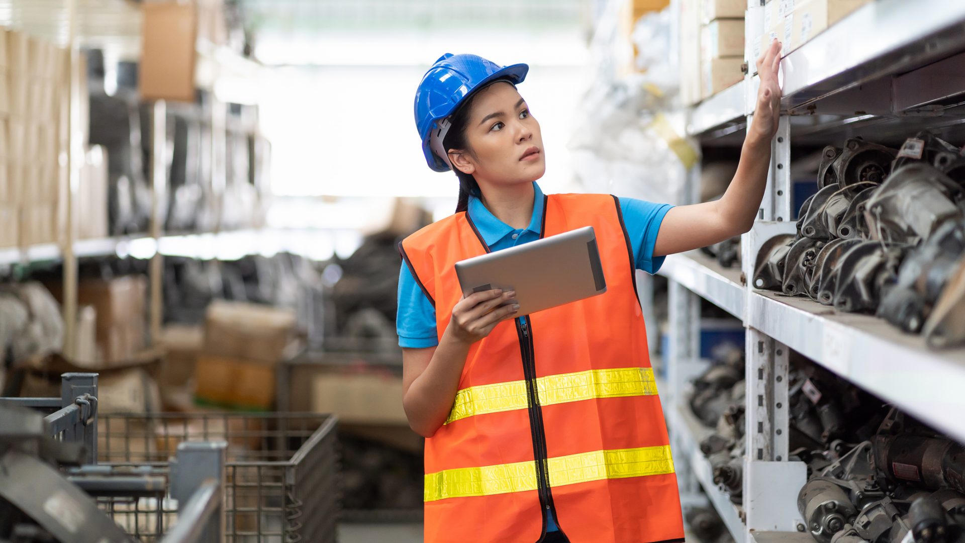 Asian young woman worker in safety vest and helmet using digital tablet for checking barcodes automotive spare parts on parcel goods on shelf pallet in industrial factory warehouse 7 Best Practices for Managing Critical Spare Parts in MRO